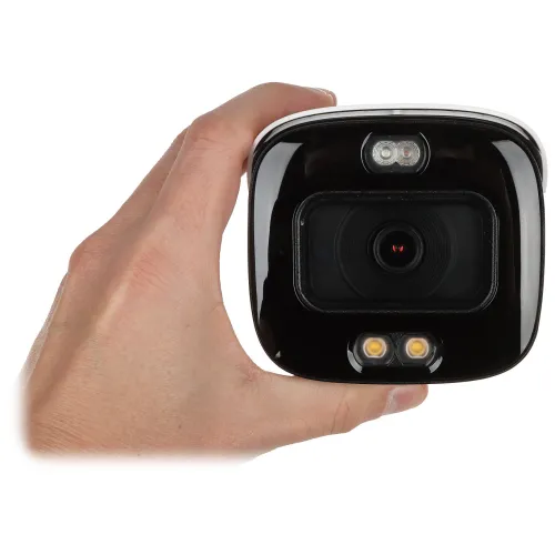 Na zdjęciu widać rękę trzymającą czarną kamerę monitoringu z dwoma diodami LED i obiektywem pośrodku. Kamera ma błyszczącą powierzchnię i jest widoczna z przodu.