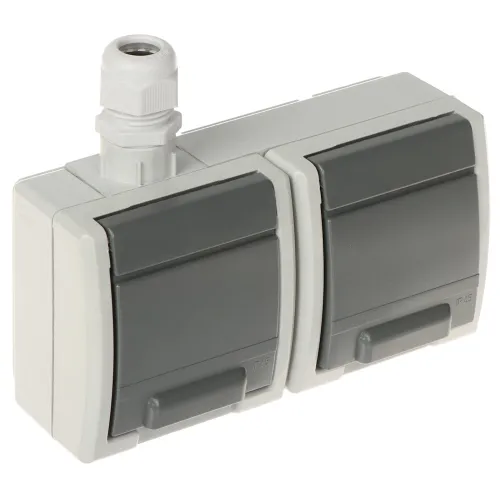 Podwójne gniazdo natynkowe z szarymi klapkami ochronnymi i białą obudową, posiadające stopień ochrony IP65. Na górze znajduje się dławik kablowy do wprowadzenia przewodów.