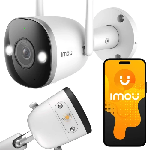 Zdjęcie przedstawia białą kamerę IP Imou IPC-F42FEP z dwoma antenami, zamontowaną na ścianie. Obok kamery widoczny jest smartfon z aplikacją Imou na ekranie.