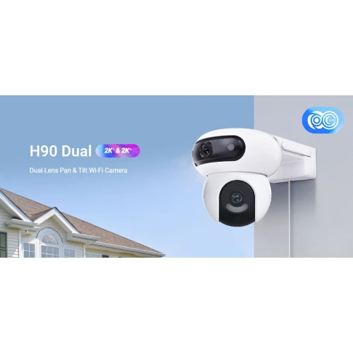 Na zdjęciu znajduje się biała, obrotowa kamera IP Wi-Fi zamontowana na zewnętrznej ścianie budynku. W tle widać fragment dachu domu oraz niebieskie niebo.