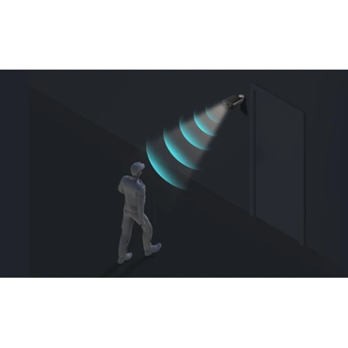 Na zdjęciu widać osobę idącą w kierunku drzwi, nad którymi zamontowana jest kamera monitoringu emitująca niebieskie fale. Scena jest utrzymana w ciemnej kolorystyce, co podkreśla działanie kamery.