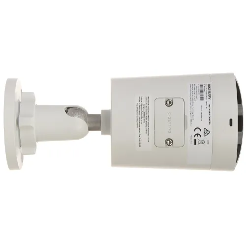 Na zdjęciu znajduje się biała kamera monitoringu zamontowana na uchwycie, widziana z boku. Kamera ma cylindryczny kształt i widoczne są na niej etykiety z informacjami technicznymi.