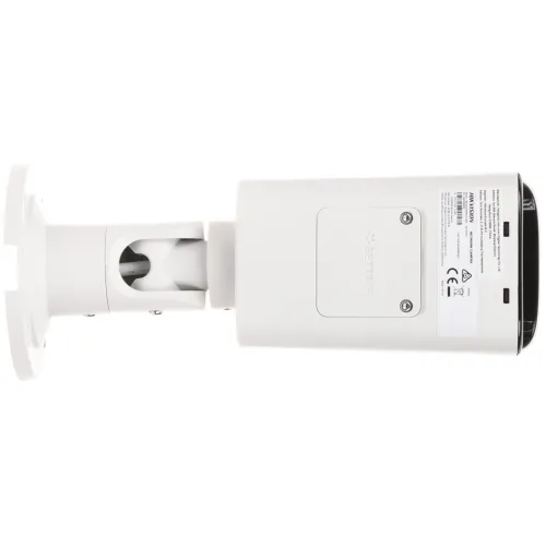 Zdjęcie przedstawia biały, prostokątny aparat monitoringu zamontowany na uchwycie, widziany od spodu. Na obudowie widoczne są etykiety z oznaczeniami technicznymi i ostrzeżeniami.