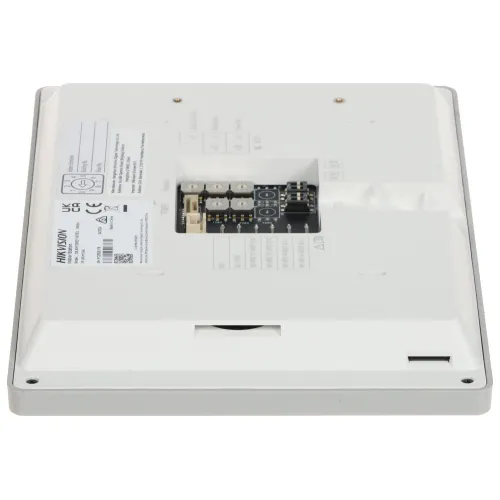 Zdjęcie przedstawia tylną część białego urządzenia elektronicznego z widocznymi złączami i etykietami. Na środku znajduje się otwór z odsłoniętymi elementami elektronicznymi.