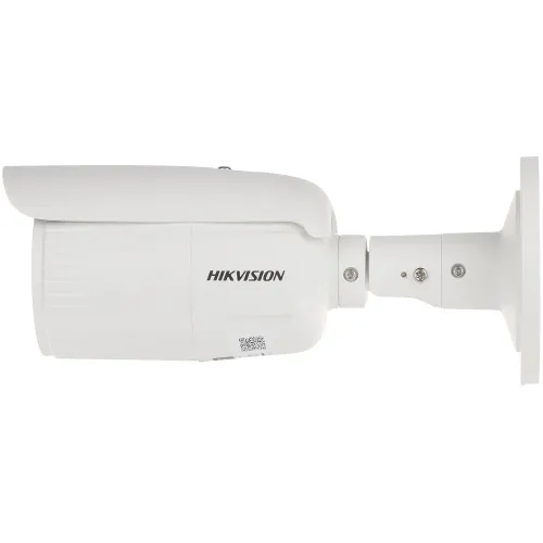 Na zdjęciu znajduje się biała kamera monitoringu marki Hikvision, widoczna z boku, zamontowana na uchwycie ściennym. Kamera ma cylindryczny kształt i widoczne logo producenta.