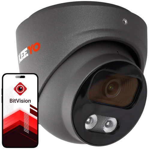 Na zdjęciu znajduje się czarna kamera monitoringu IP marki KEEYO z widocznym obiektywem i diodami LED, obok której pokazany jest smartfon z aplikacją BitVision. Kamera ma nowoczesny, kompaktowy design, a aplikacja na ekranie telefonu prezentuje logo i czerwono-biały interfejs.
